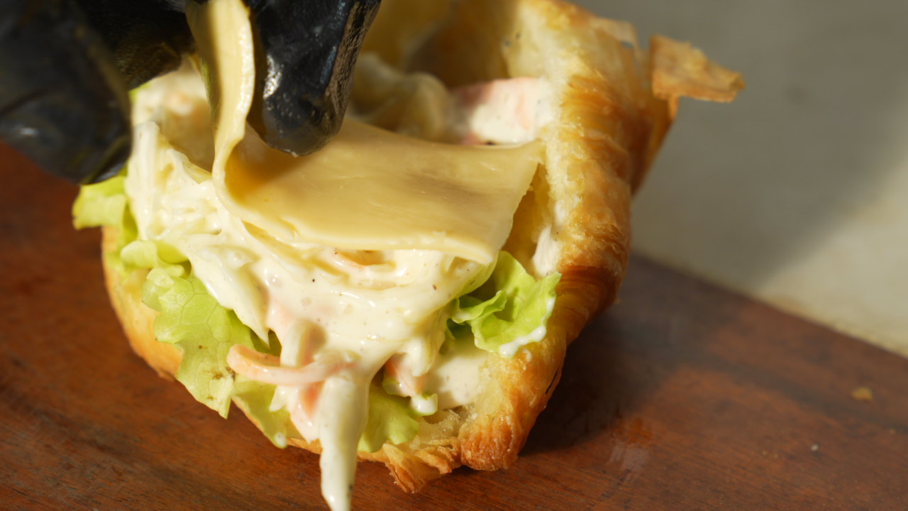 Cheese and sauce being layered onto a stuffed croissant